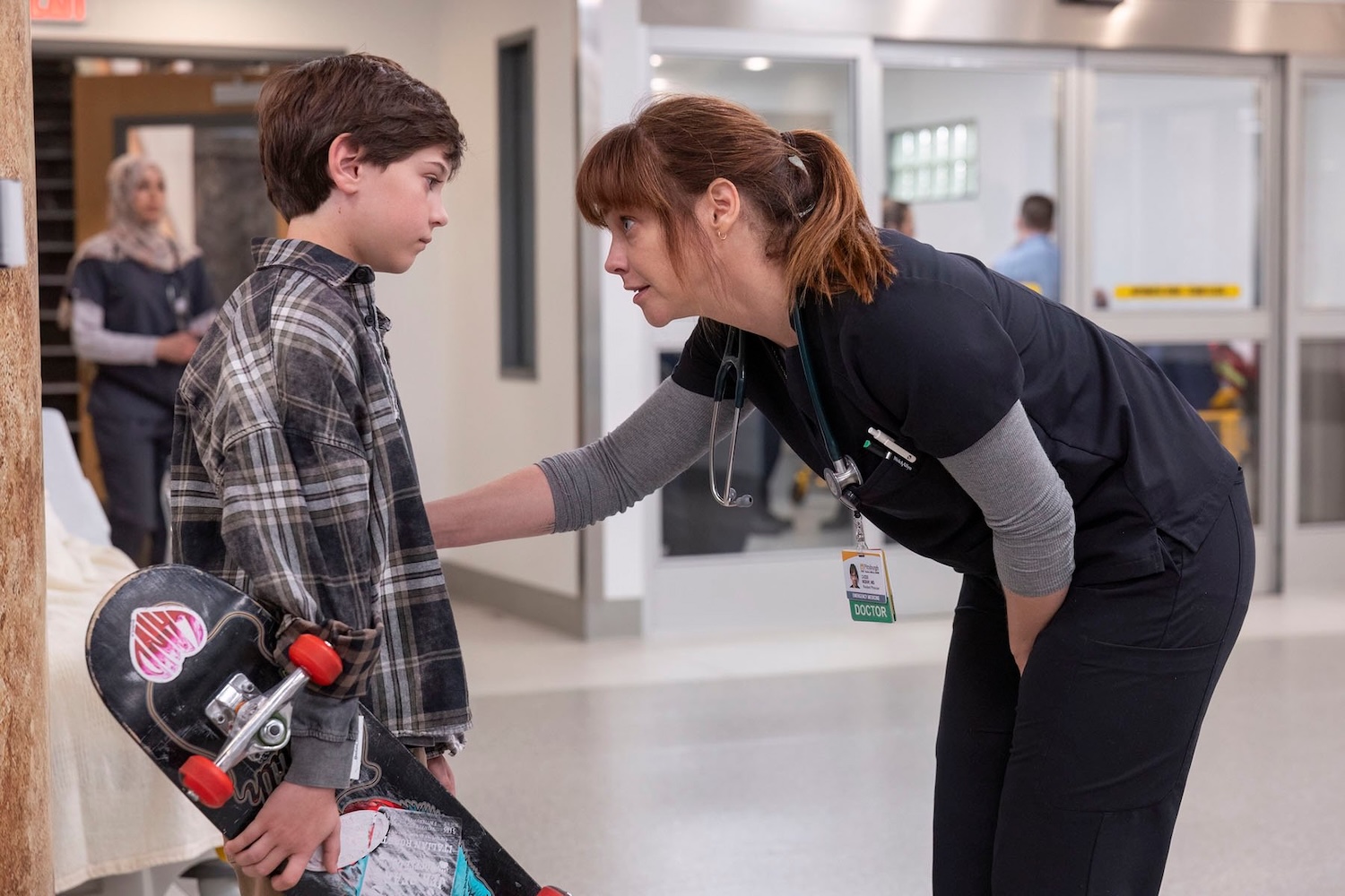 A character on "The PItt" speaks with a young boy holding a skateboard in a hospital.