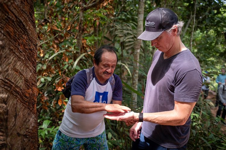 An Indigenous man in the Brazilian Amazon shows something to California Gov Gavin Newsom by placing it in his outstretched hand