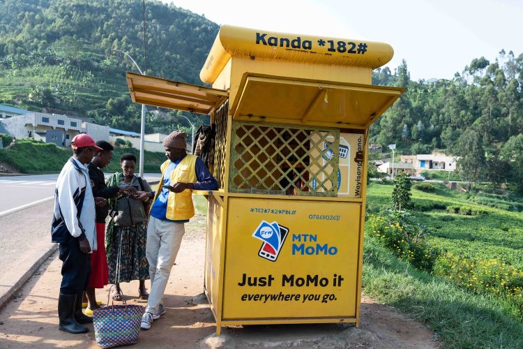 People speak to an agent at a yellow MoMo Mobile Money kiosk in Rwanda.