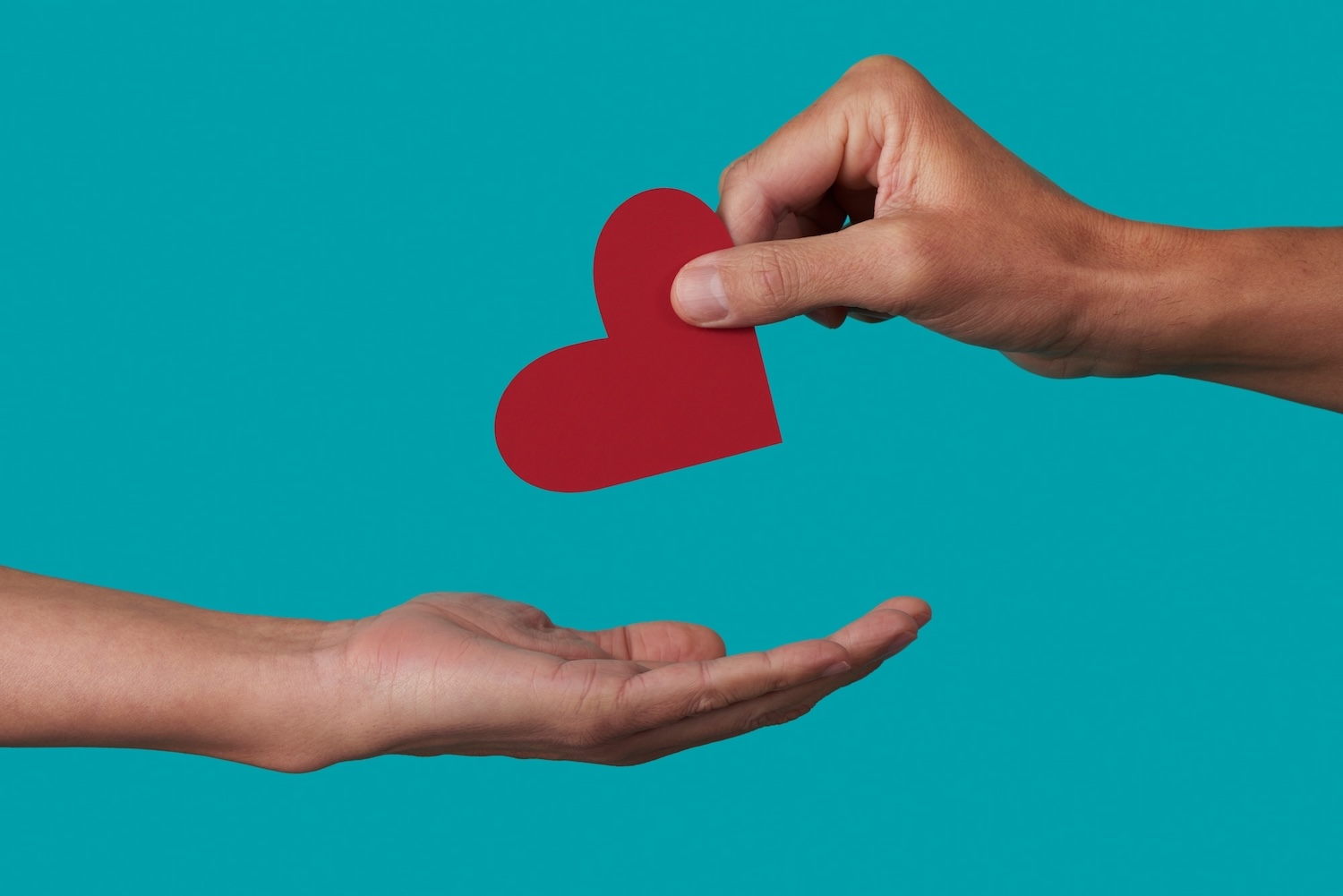 A person holding a paper cutout of a heart passes it along to along to another person.