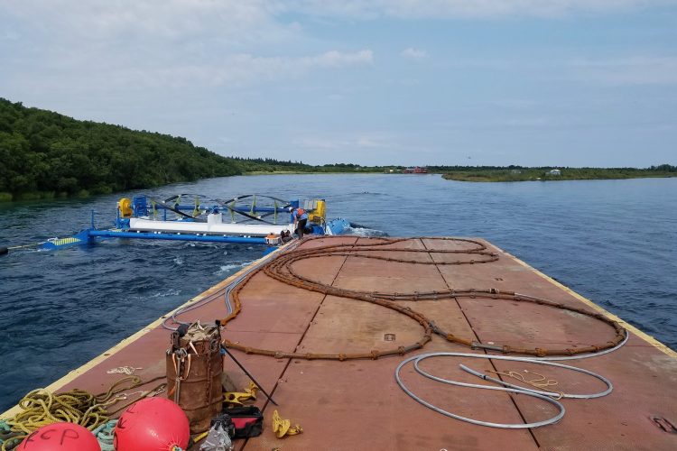 A river barge floats next to the RivGen river turbine, also floating in the water of the Kvichak River.