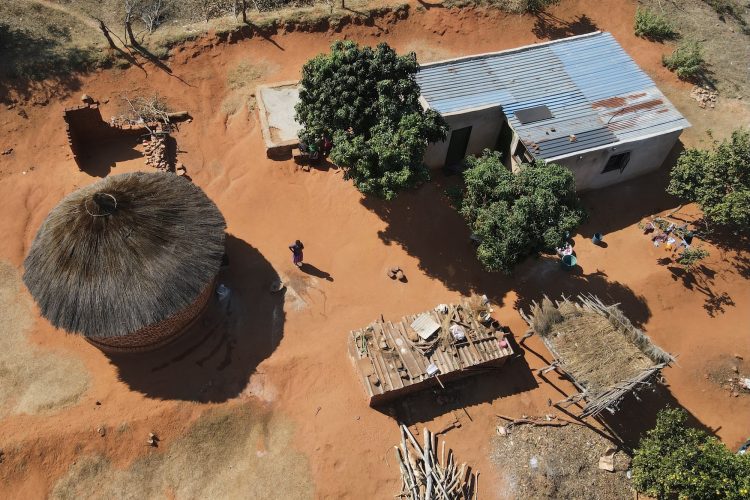 An overhead view of Esther Mwedzi walking across her yard between her separate kitchen building and her home.