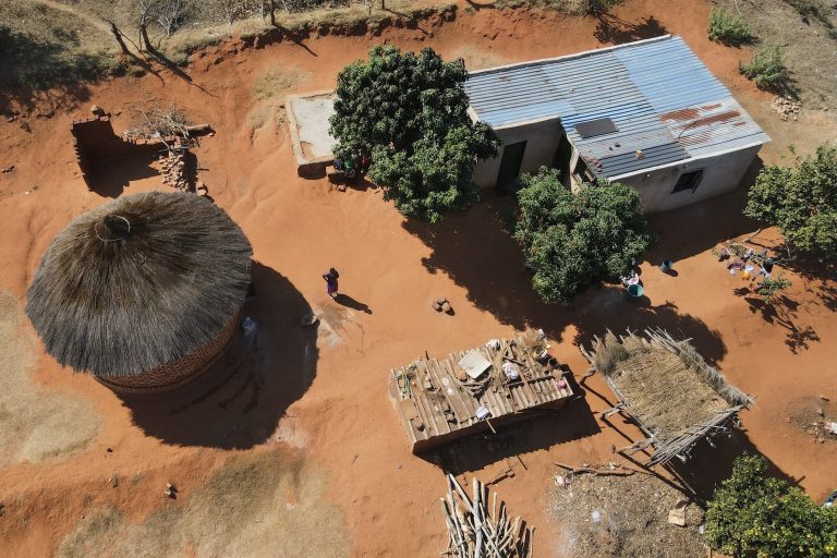 An overhead view of Esther Mwedzi walking across her yard between her separate kitchen building and her home.