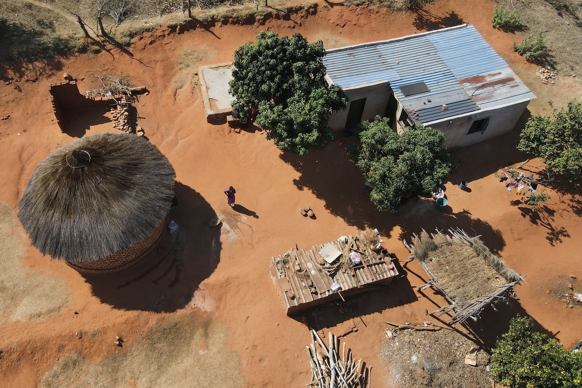 An overhead view of Esther Mwedzi walking across her yard between her separate kitchen building and her home.