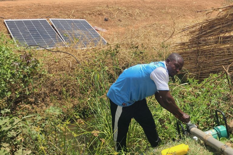 A farmer turns the faucet to start the flow of water on a pump powered by nearby solar panels.