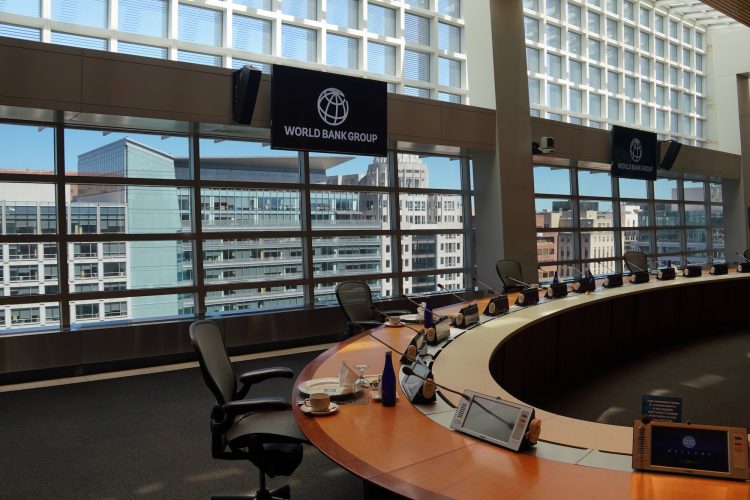 A meeting room with screens that read "World Bank Group" features a large circular conference table with microphones and tablets prepared for meeting attendees.